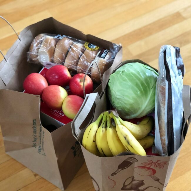 Es ist sind zwei Einkaufstaschen mit Obst und Gemüse zu sehen. Man sieht Brötchen, Äpfel, Bananen und ein Stück Kopfkohl.